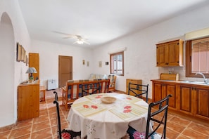 Un comedor con una mesa redonda, sillas, un ventilador de techo y una cocina con armarios de madera y un ventanal.