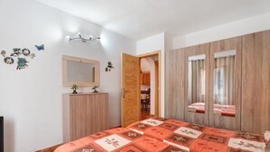 Ein Schlafzimmer mit Bett, Kleiderschrank, Spiegel und einer Tür zu einem anderen Raum.