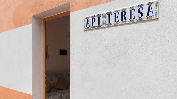 Ein Schild mit der Aufschrift 'APT TERESA' an einer weißen Wand.