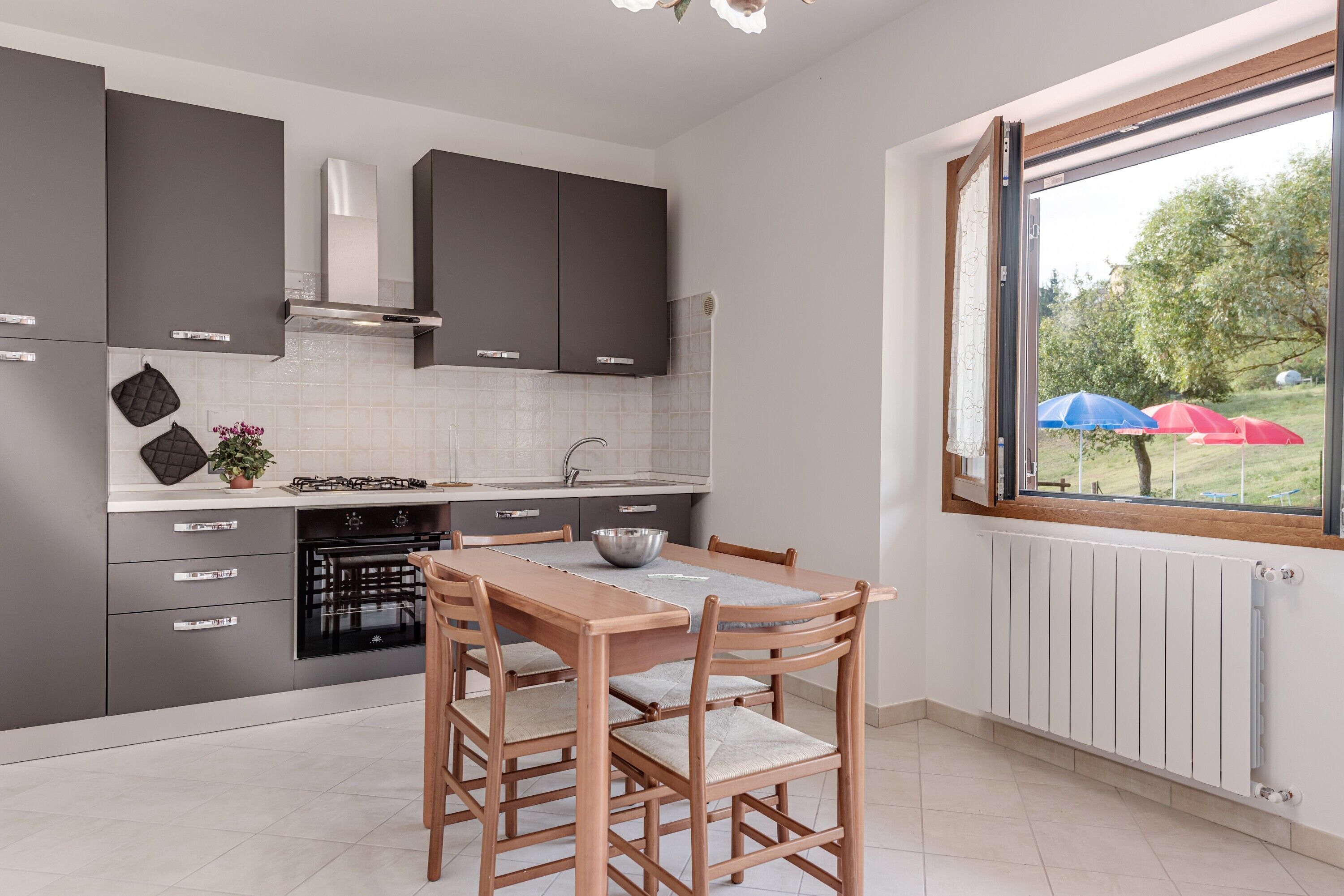 Una cucina moderna con mobili grigi, un tavolo da pranzo in legno e vista su un giardino attraverso una finestra.