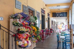 A corridor with a floral display, red chairs, and tables, and signs indicating rooms and a piano.