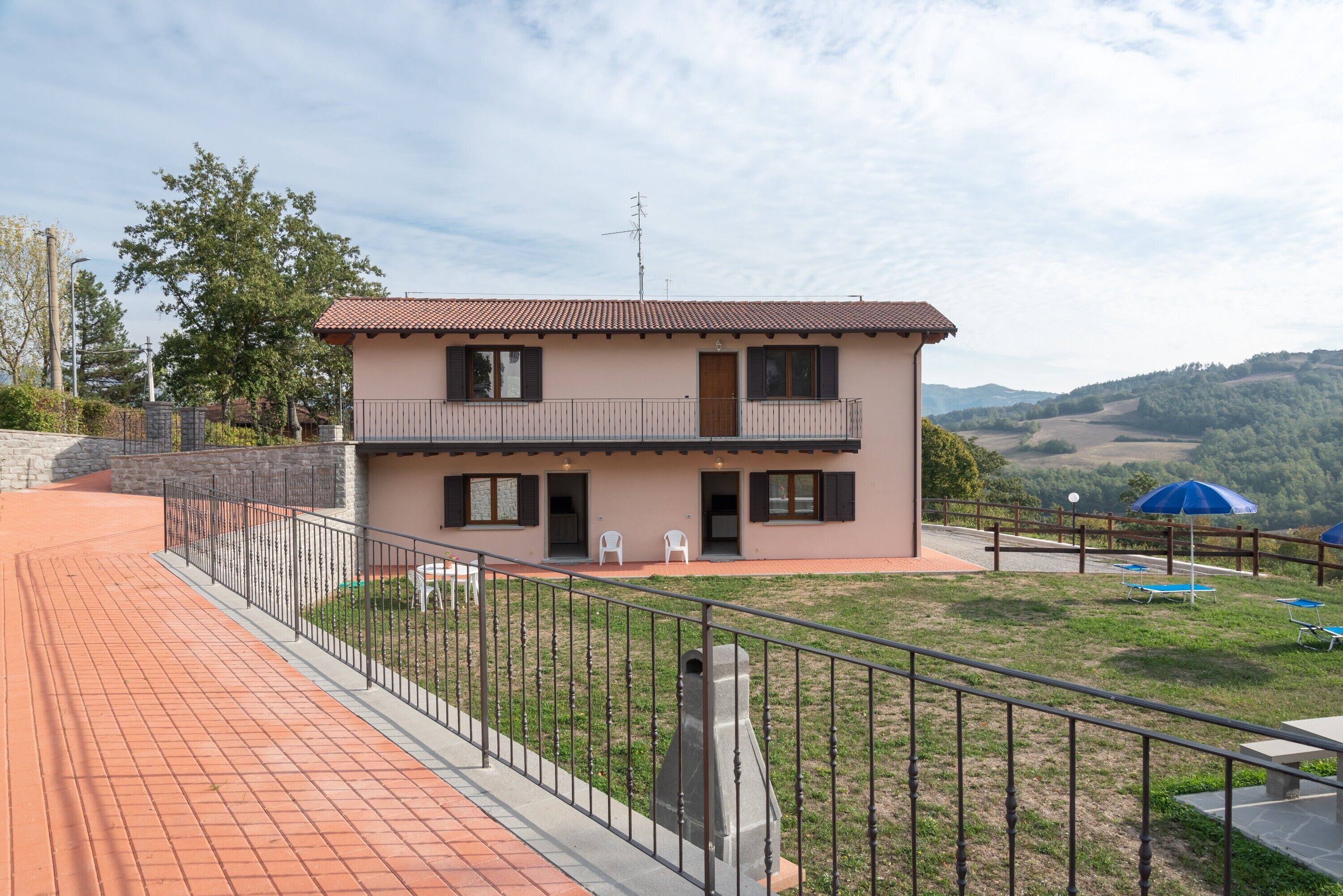 A two-story building with a balcony, a paved walkway, and a grassy area with outdoor furniture.