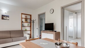 Un soggiorno moderno con divano, tavolo da pranzo, televisore e libreria.