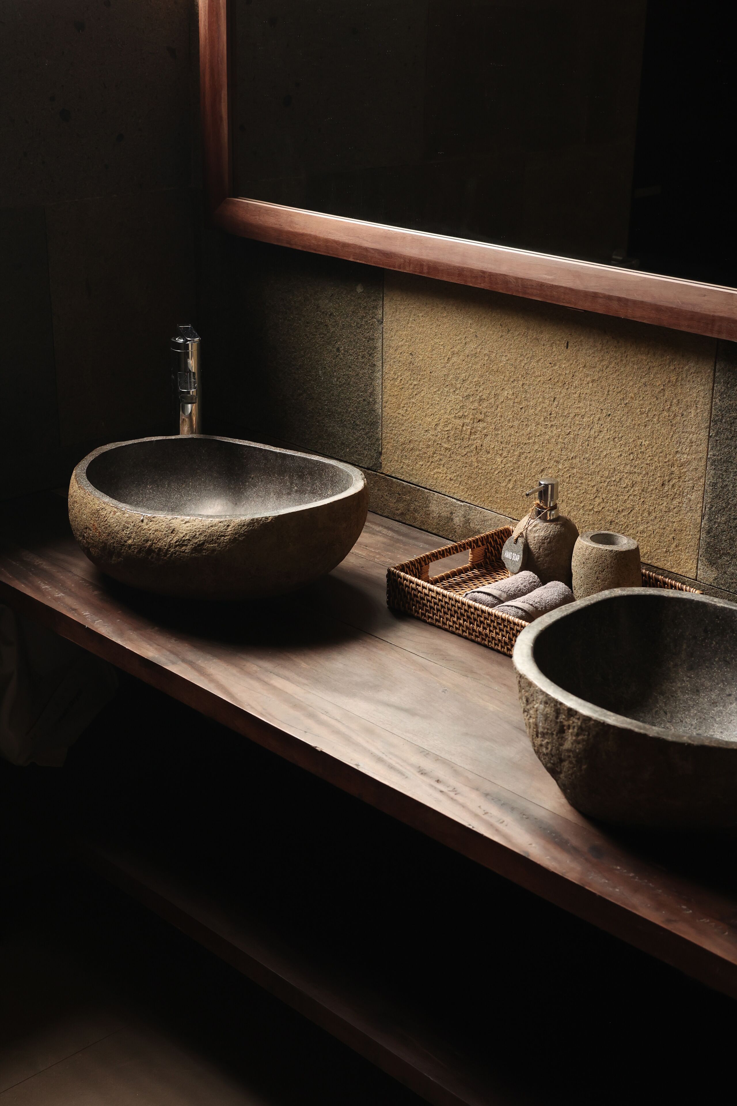 Une salle de bain avec un grand lavabo en pierre de forme ronde, un petit plateau en bois contenant des serviettes et un grand récipient en pierre.