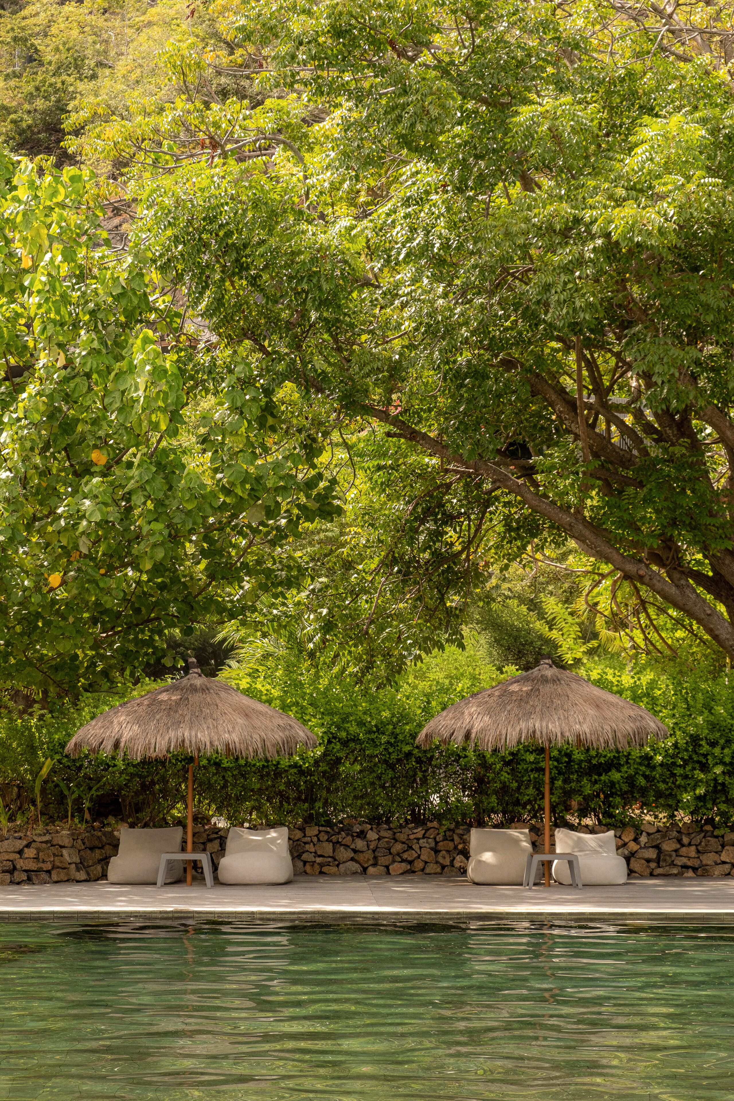 A pool area with two thatched umbrellas and white lounge chairs.