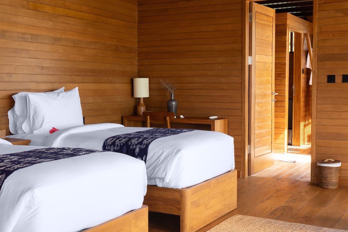 A wooden room with two beds, a nightstand, a lamp, and a vase.