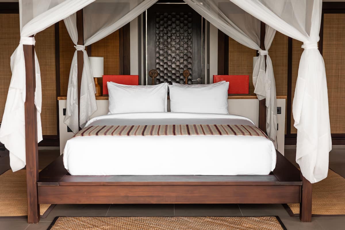 A bed with a canopy, a wooden headboard, and two nightstands with red cushions.