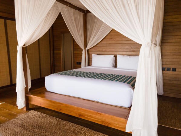 Een slaapkamer met een houten bedframe, witte beddengoed en een hemelbed.