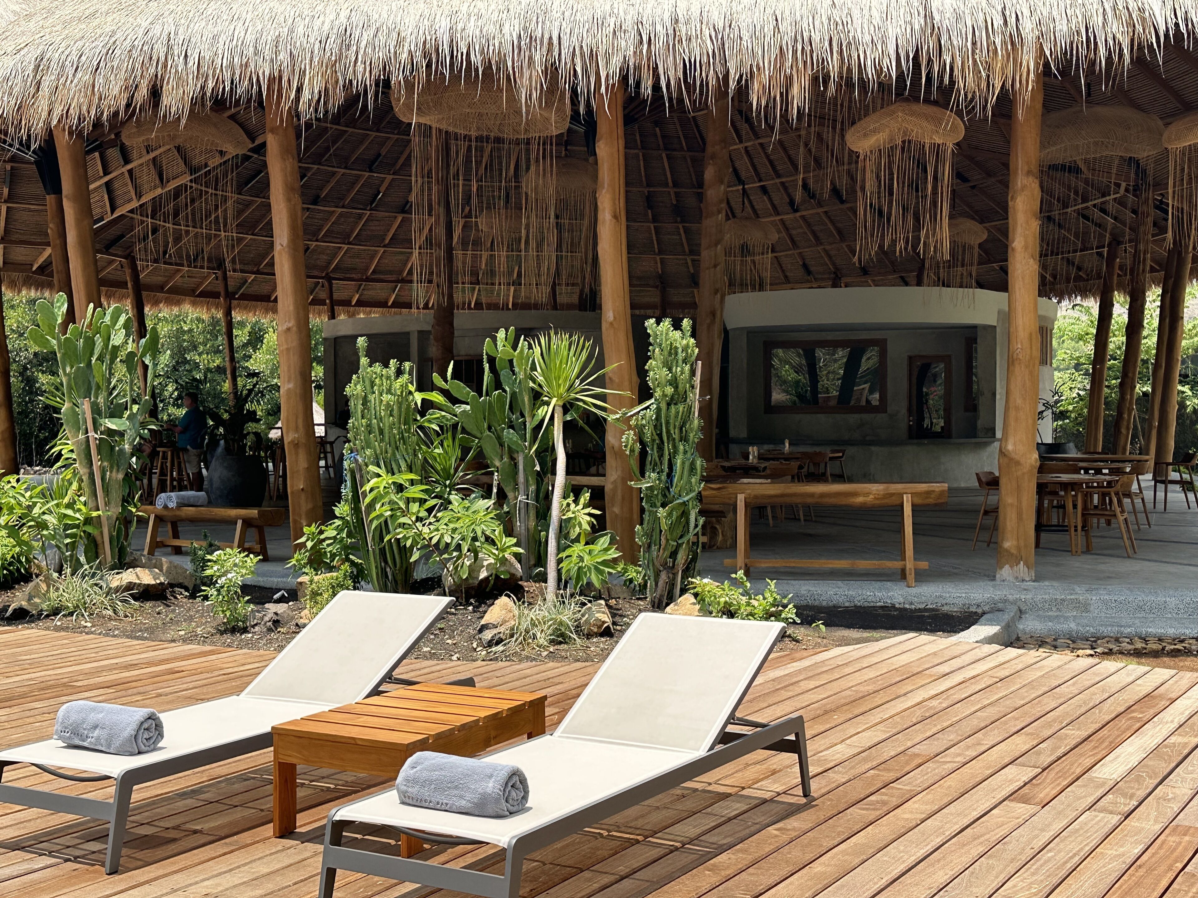 A wooden deck with lounge chairs and a thatched roof structure.