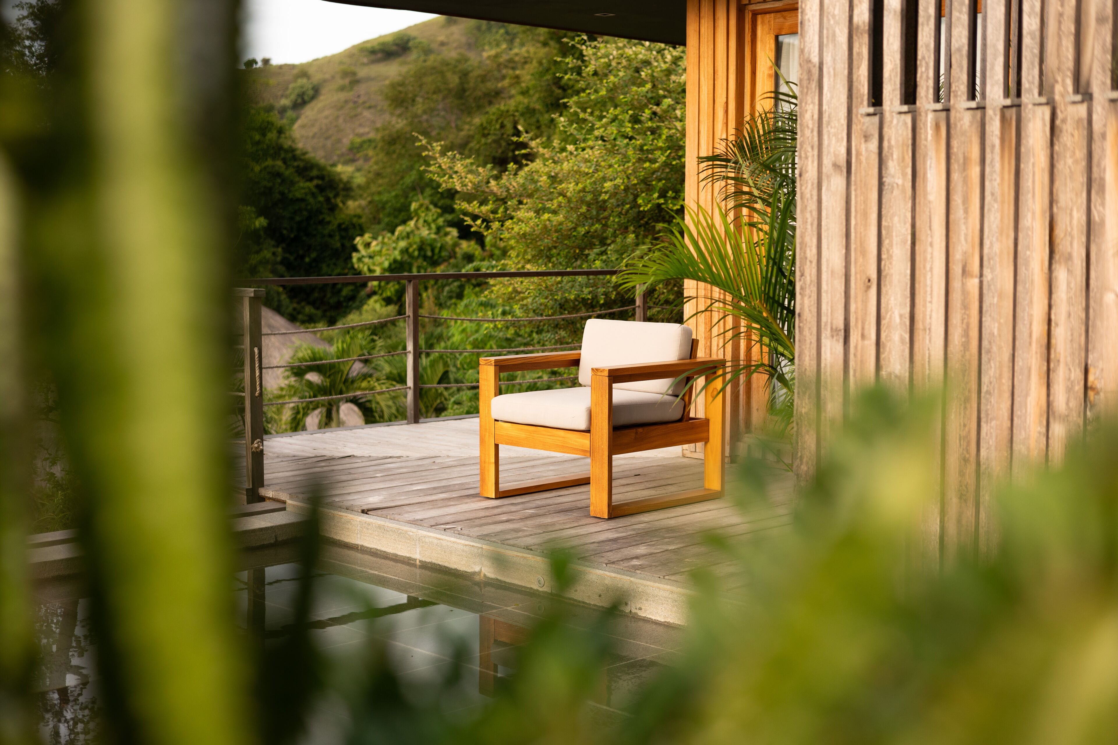 A wooden deck with a single chair, a railing, and a view of a lush green hillside.