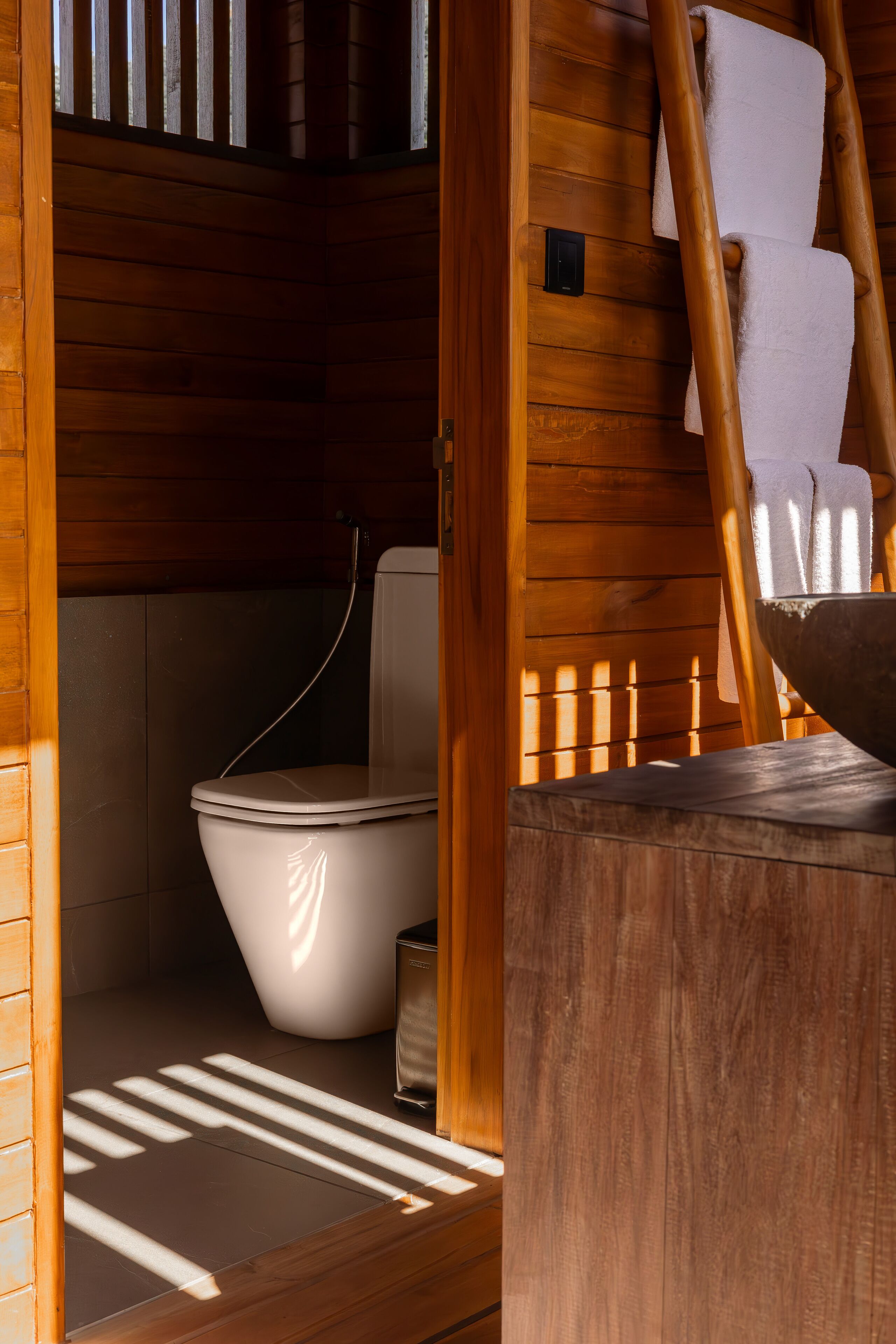 Innenansicht einer Holzhütte mit Toilette, einem Holzvorderschrank und einem Handtuchhalter.