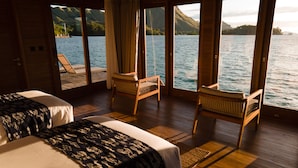 Una habitación con dos camas, suelo de madera y grandes ventanales con vistas al agua.