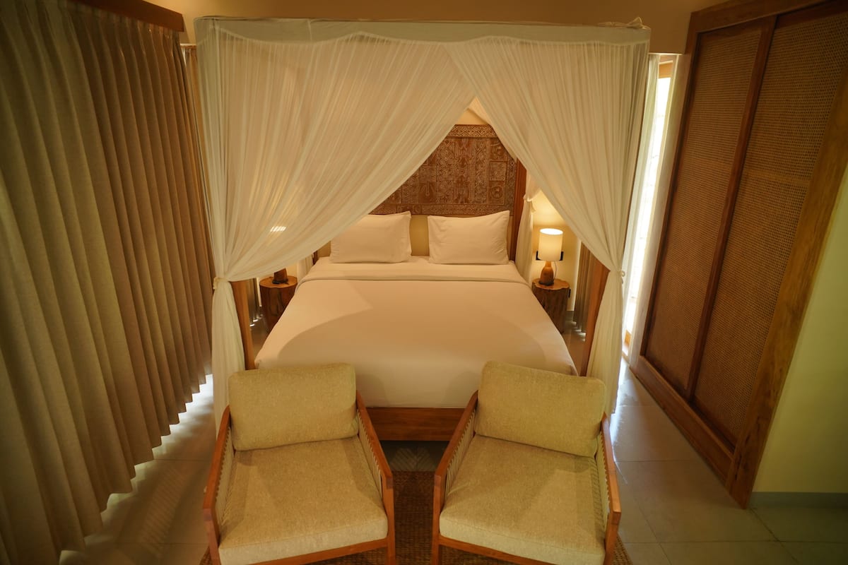 A room with a bed, two chairs, a nightstand, and a lamp.