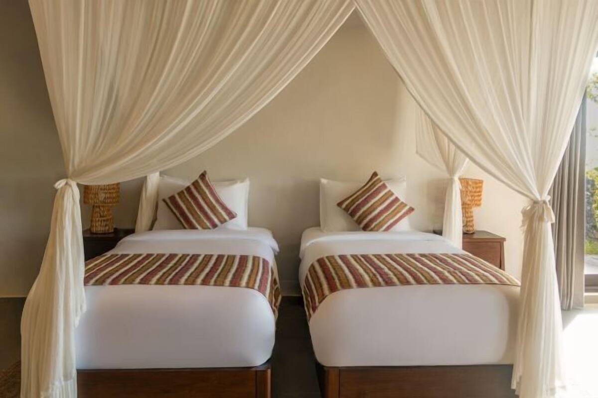 A room with two beds, each with striped bedding and pillows, and a canopy over the beds.