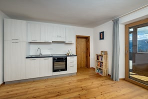 A modern kitchen with white cabinets, a built-in oven, and a wooden floor.