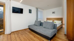 Ein modernes Schlafzimmer mit Schlafsofa, Einzelbett, Holzboden und einem großen Fenster mit Vorhängen.