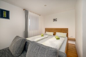 A hotel room with two beds, a sofa, a wooden headboard, a small picture on the wall, and a window with curtains.