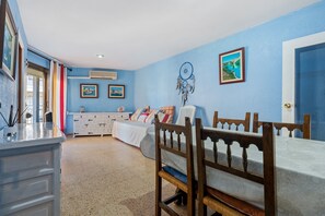 A bedroom with a bed, a desk, and a chair. There is a window with curtains, a wall with a dreamcatcher, and a picture frame.