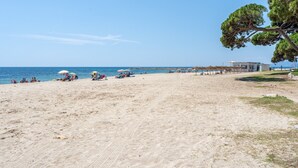 Une plage avec des gens, des parasols et un bâtiment d’où l’on peut admirer la mer.