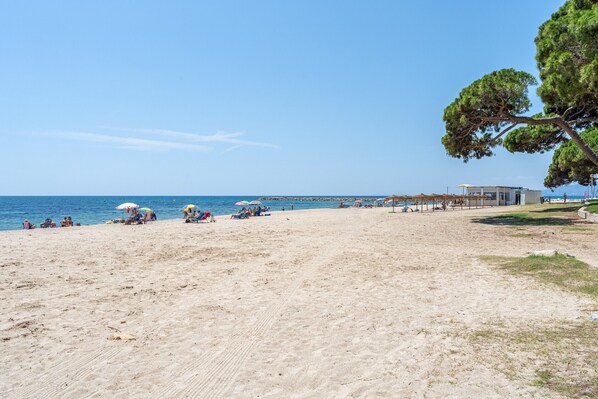 A beach with people, umbrellas, and a building with a view of the sea.