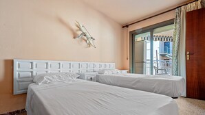 A hotel room with two beds, a white headboard, a decorative wall piece, and a view of the outside. - Apartment 'Two Minutes from the Sea' with Partial Sea Views, Terrace, and Air Conditioning (Cambrils)