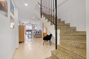 A staircase with a metal railing, a living room with a sofa and a chair, and a kitchen area in the background.