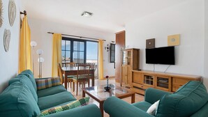 Un salon avec deux canapés verts, un meuble en bois, un téléviseur et un coin repas comprenant des chaises et une table.