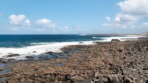 Une côte rocheuse où les vagues s’écrasent contre les rochers, un ciel bleu dégagé et une terre lointaine à l’horizon.