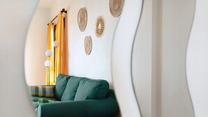 Une pièce avec un canapé vert, une petite table ronde et des œuvres d’art décoratives accrochées au mur.