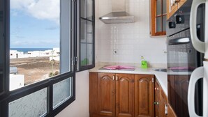 Une cuisine dotée de meubles en bois, d’une hotte de cuisinière en acier inoxydable, d’une fenêtre donnant sur la mer et d’un dosseret de carreaux blancs.