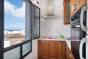 Una cocina con armarios de madera, una campana extractora de acero inoxidable, una ventana con vistas al mar y un salpicadero de azulejos blancos.