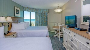 Ein Hotelzimmer mit zwei Betten, einem Fernseher, einem Schreibtisch mit Stuhl und Blick auf den Ozean.
