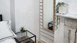 Quarto com cama, mesa de cabeceira com planta, espelho e prateleira pequena com planta.