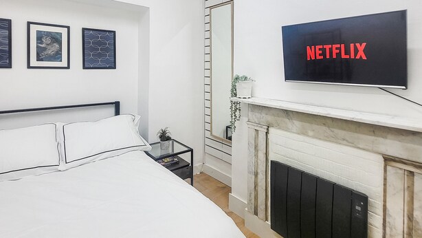 Um quarto moderno com uma cama, uma TV fixada na parede e uma lareira.