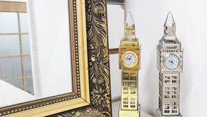 Um espelho com moldura dourada ornamentada e dois modelos em miniatura do Big Ben.