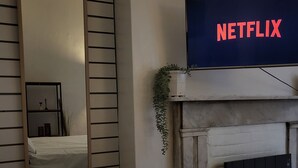 Quarto com cama, espelho, lareira e televisão exibindo o logotipo da Netflix.