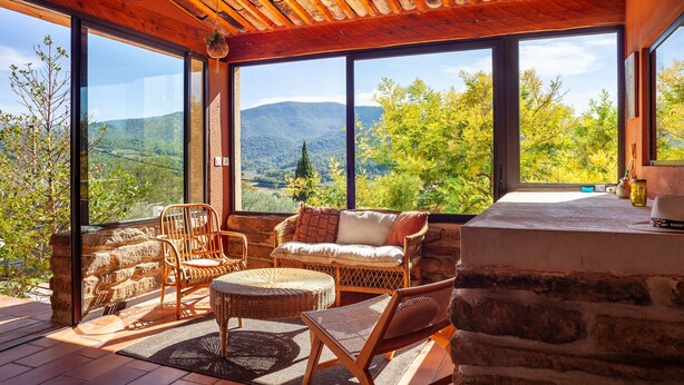 A room with large windows, wicker furniture, and a stone wall. - Holiday Home 'La Bastide Des Oliviers' with Mountain View, Wi-Fi and Air Conditioning (Auriol)