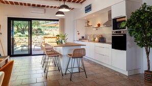A modern kitchen with a central island, bar stools, a large potted plant, and a view of the outdoor patio. - Holiday Home 'La Bastide Des Oliviers' with Mountain View, Wi-Fi and Air Conditioning (Auriol)