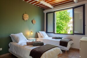 Un dormitorio con dos camas, una ventana con vistas a la vegetación, una lámpara de noche y un objeto decorativo en la pared.