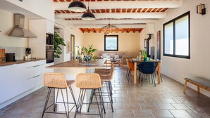 A modern kitchen with a central island, bar stools, a dining area with a table and chairs, and a large window providing natural light. - Holiday Home 'La Bastide Des Oliviers' with Mountain View, Wi-Fi and Air Conditioning (Auriol)