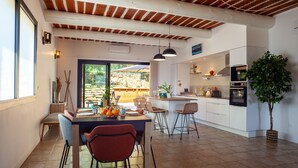 A modern kitchen with white cabinets, a dining area with a wooden table and chairs, and a large window with a view of greenery. - Holiday Home 'La Bastide Des Oliviers' with Mountain View, Wi-Fi and Air Conditioning (Auriol)