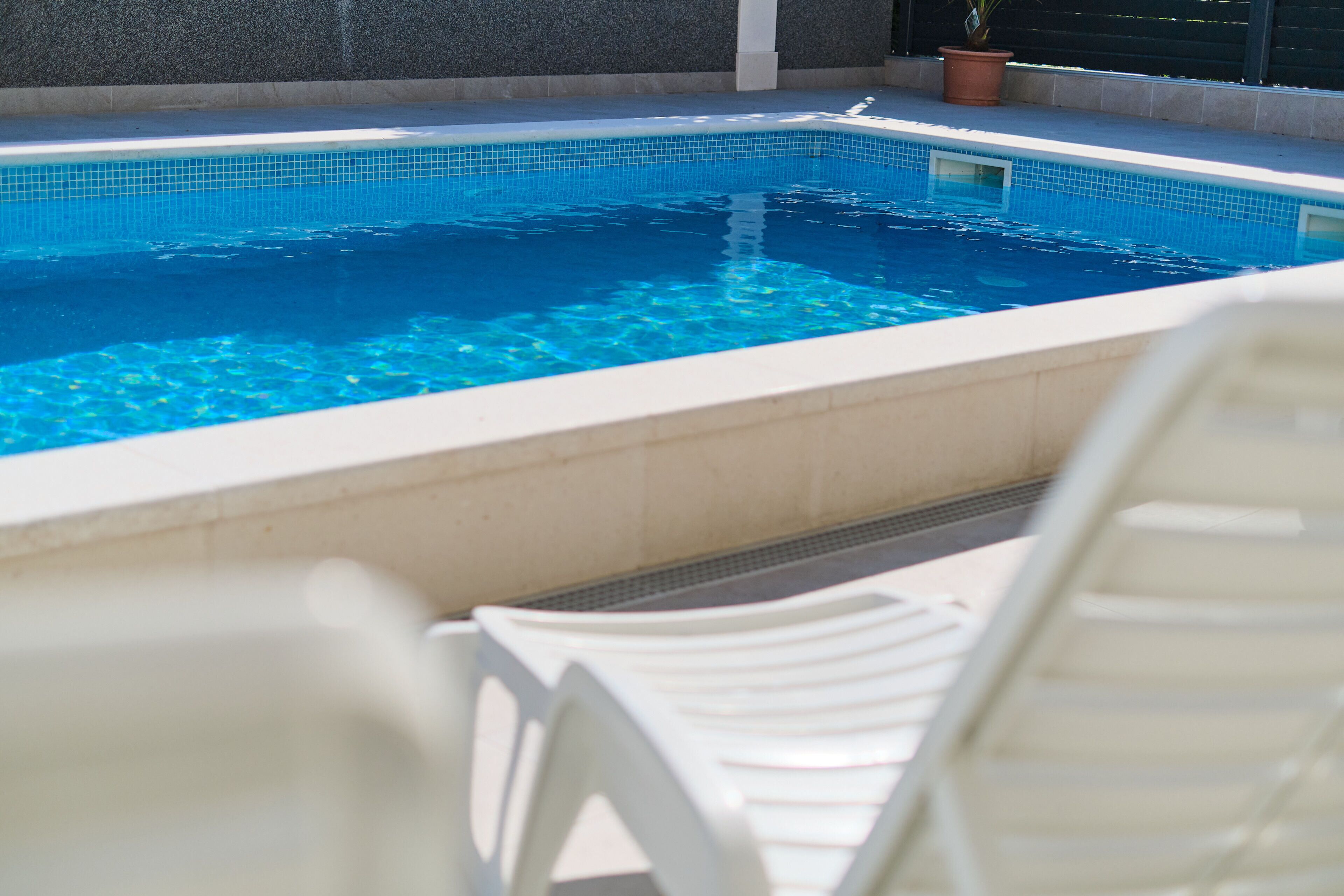 Una piscina con agua azul cristalina, rodeada de sillas reclinables blancas.