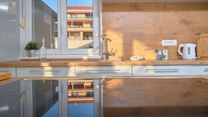 A modern kitchen with a wooden countertop, a sink, a kettle, and a window with a view of a building.