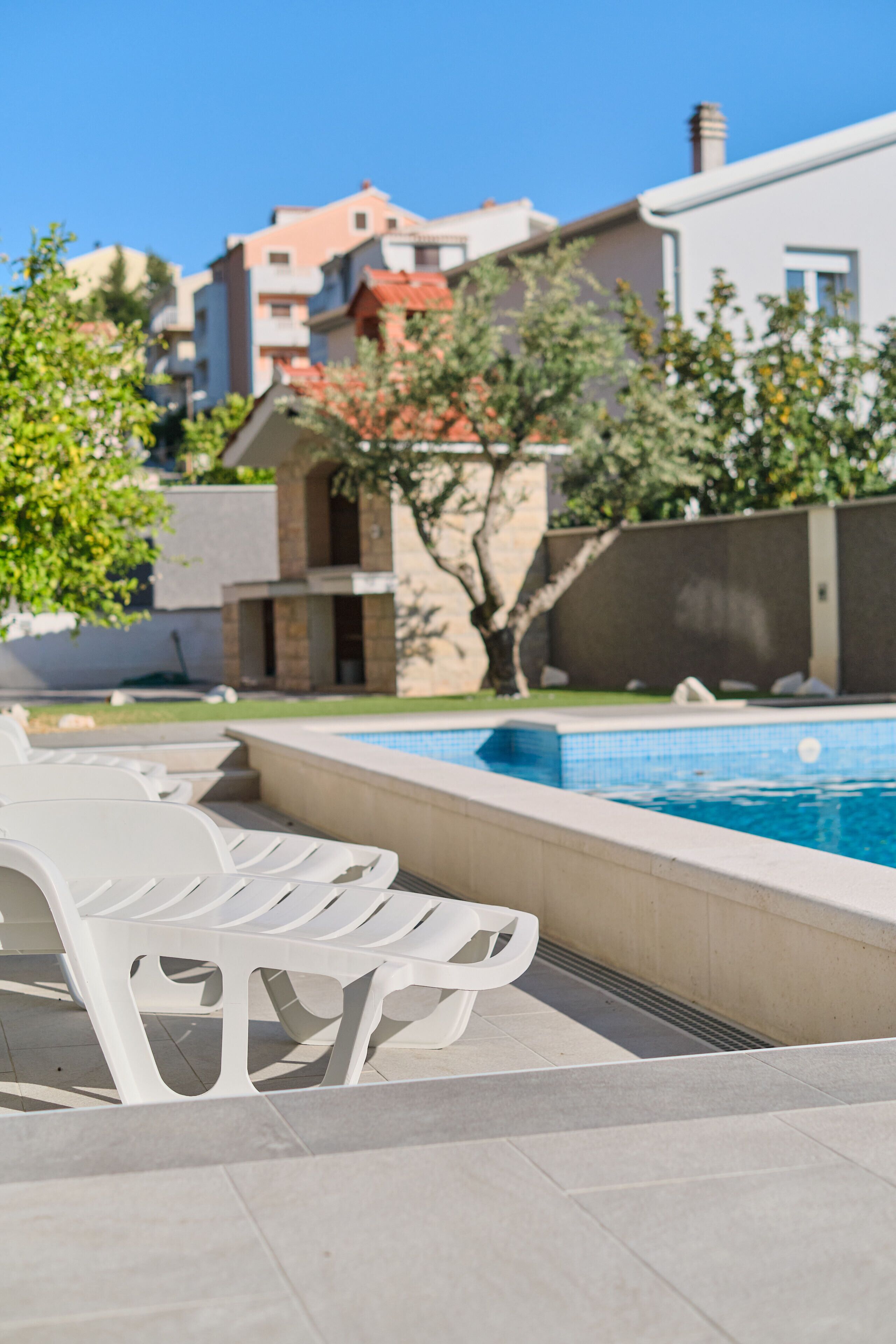 A swimming pool with lounge chairs, a tiled deck, and modern buildings in the background.