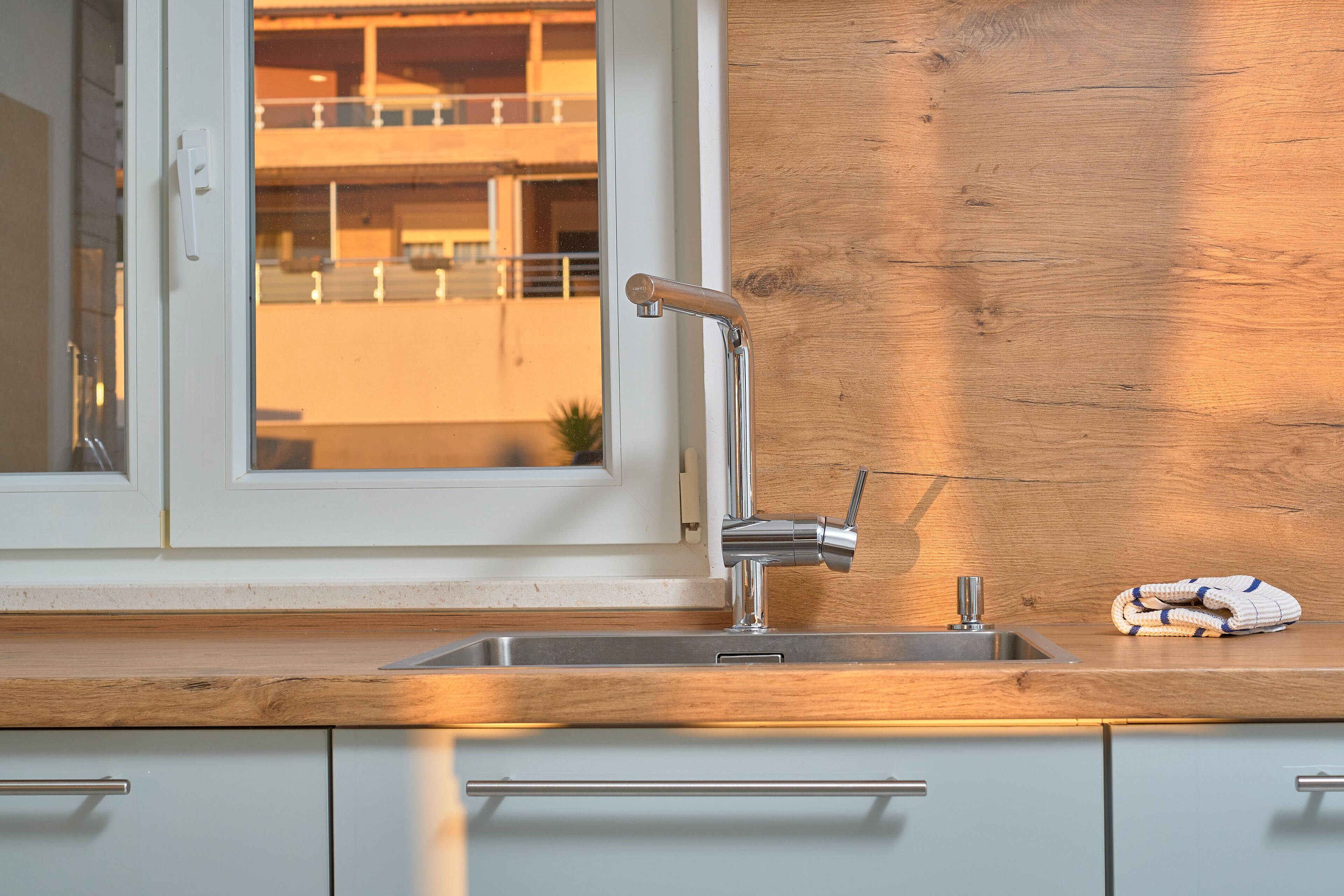 A kitchen with a stainless steel sink, a wooden countertop, and a window with a view of a building.