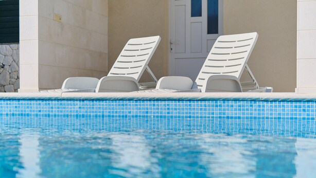 A pool with two white lounge chairs and a stone wall.