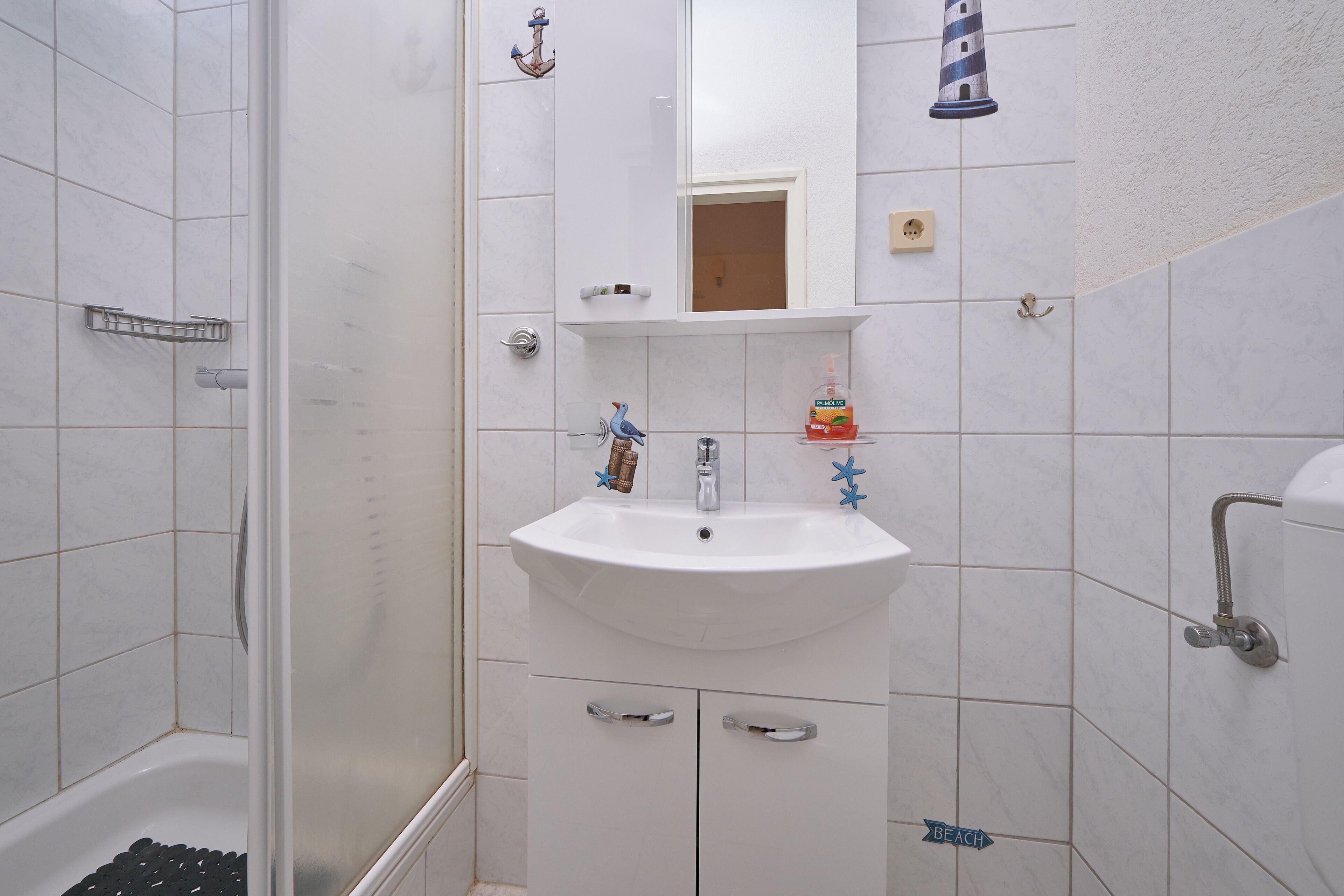 Une salle de bain avec un lavabo blanc, un miroir et un espace douche.
