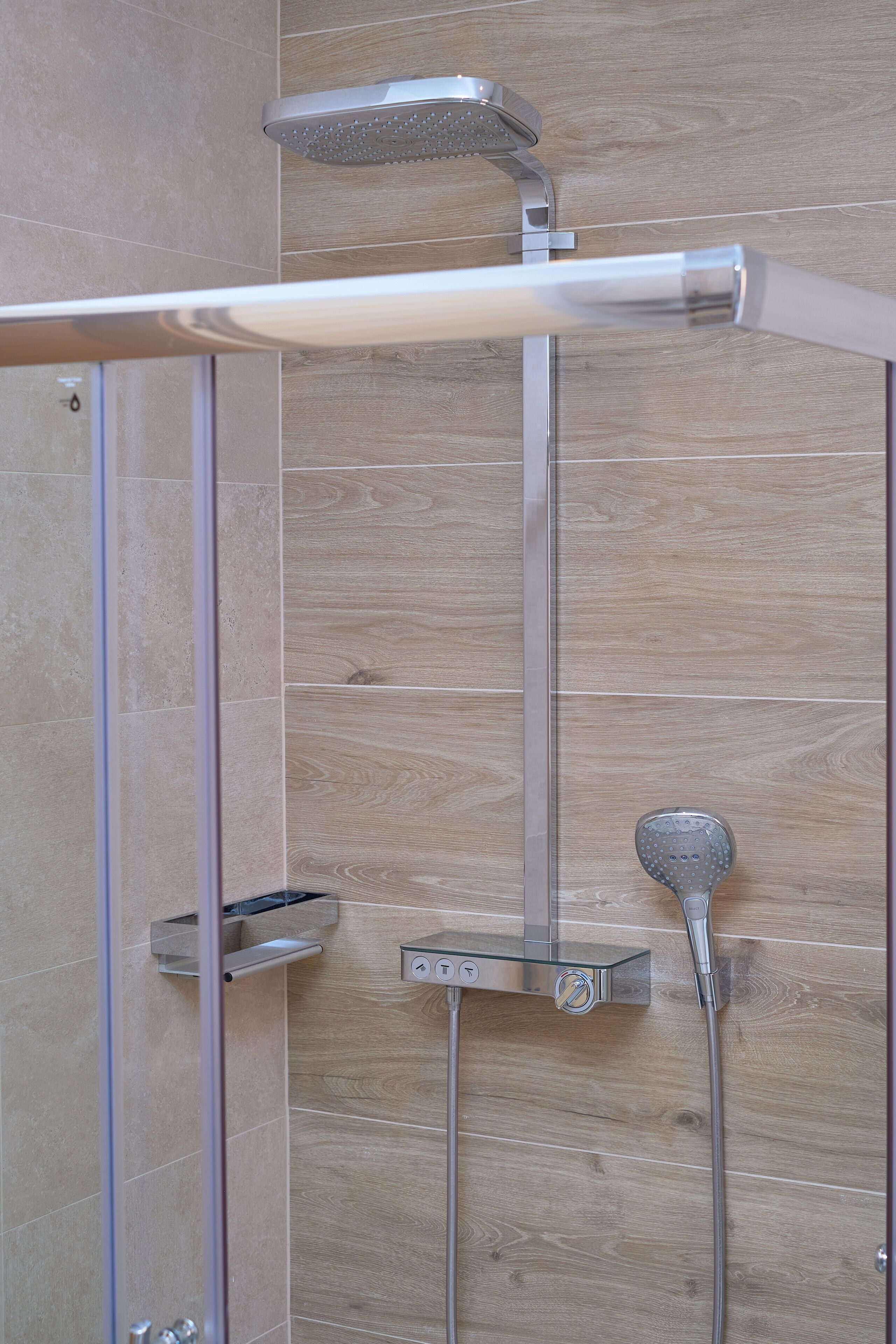 A shower area with a glass-enclosed tub, a handheld showerhead, and a wall-mounted showerhead.