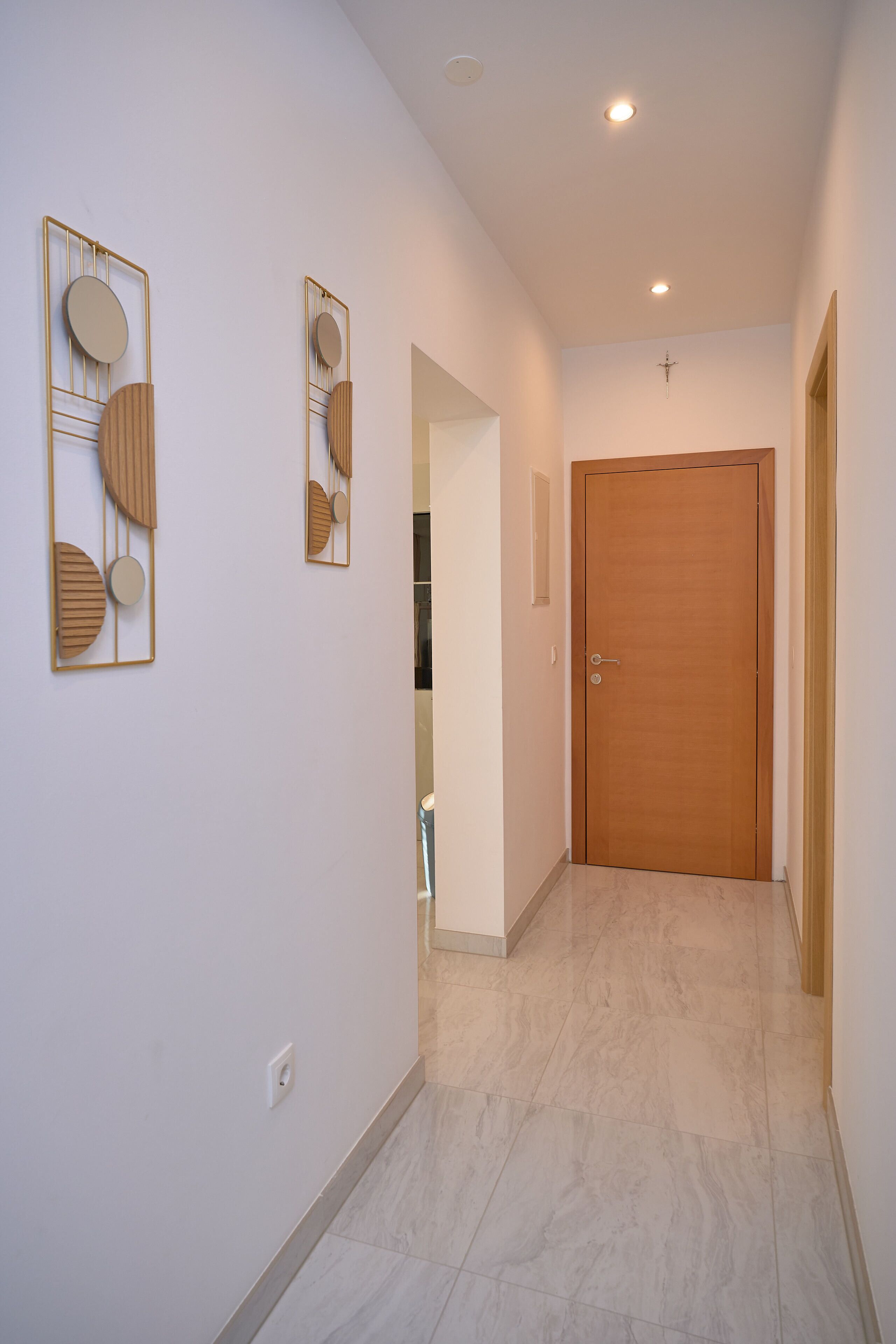 A hallway with a wooden door, a cross on the wall, and abstract wall art.