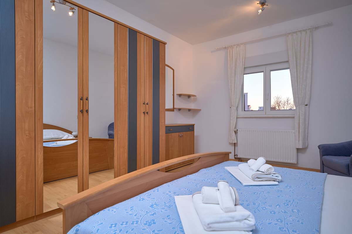 A bedroom with a bed, a wardrobe, a mirror, a window with curtains, and a chair.